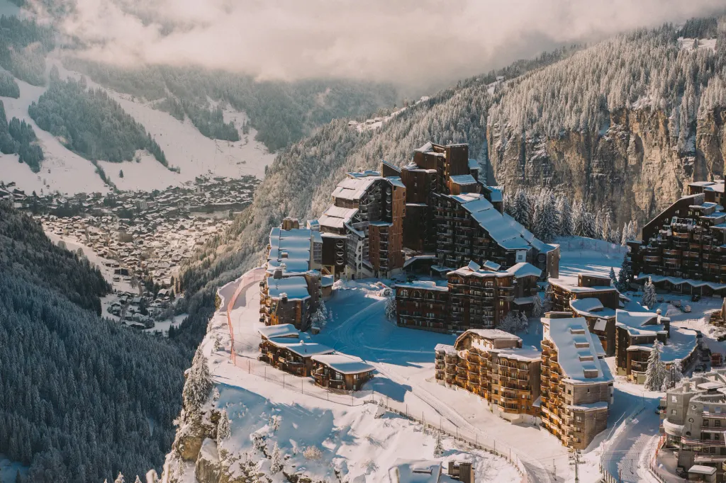 Zaśnieżone drewniane budynki Avoriaz na skraju klifu, w dole dolina z Morzine i zalesione stoki