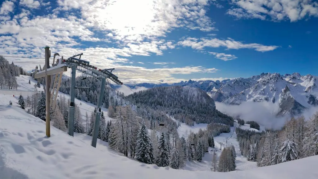 Kolej krzesełkowa w Forni di Sopra wśród ośnieżonego lasu, w tle szczyty Dolomitów Friulijskich