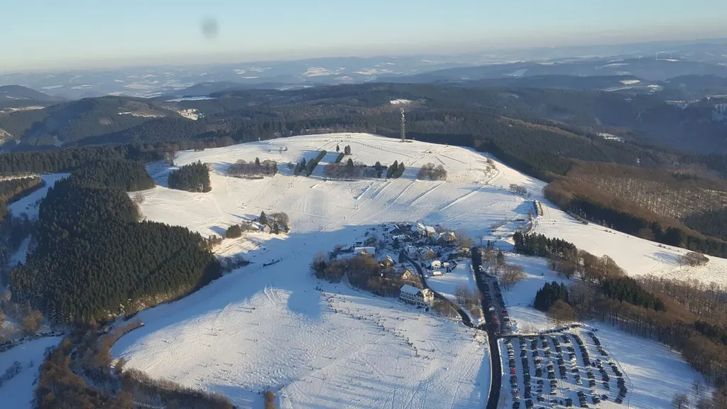 Ośrodek Wildewiese z lotu ptaka zimą, zaśnieżone stoki nad wioską i zalesione wzgórza Sauerlandu