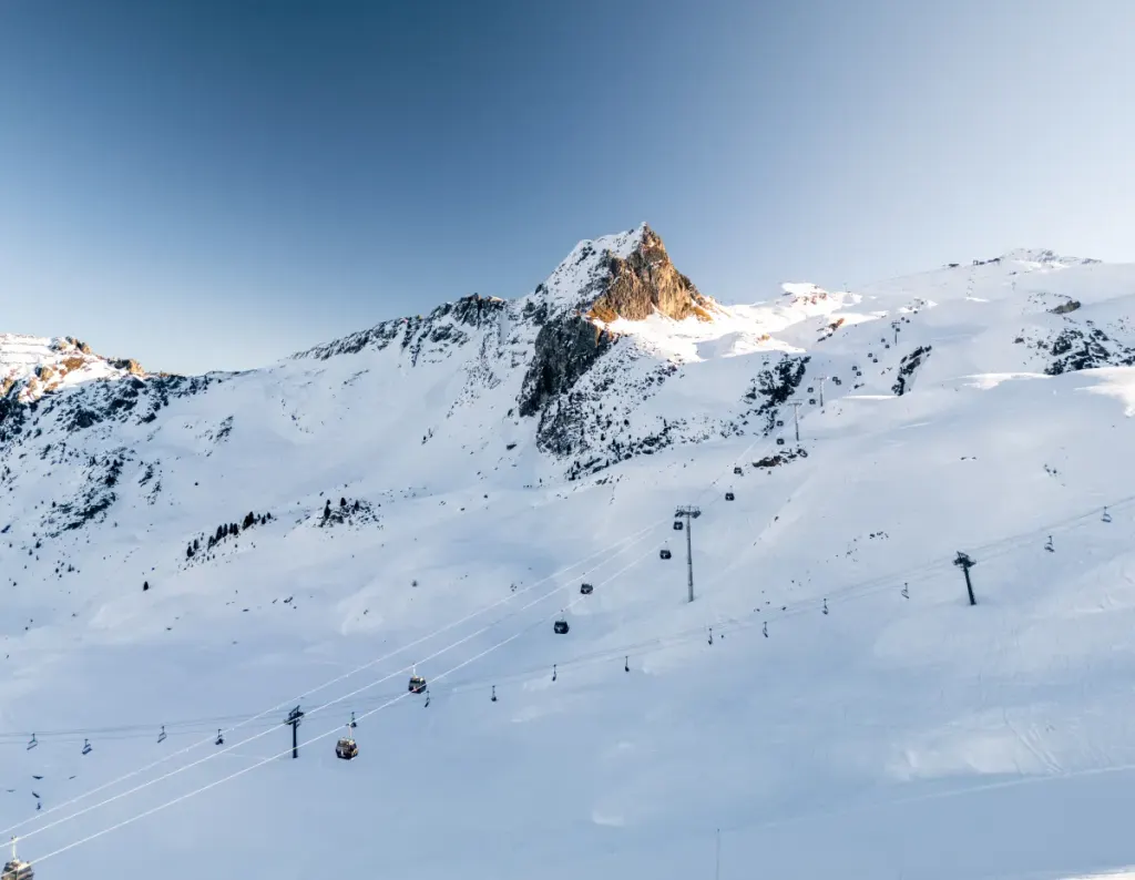 Gondola Roche de Mio nad ośnieżonymi stokami La Plagne, wyżej skalisty szczyt w porannym słońcu