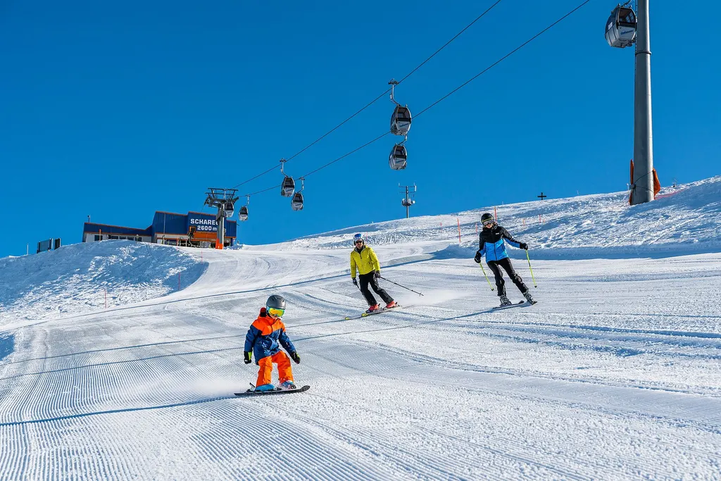 Narciarze i mały snowboardzista na ratrakowanej trasie pod gondolą przy stacji Schareck w Heiligenblut