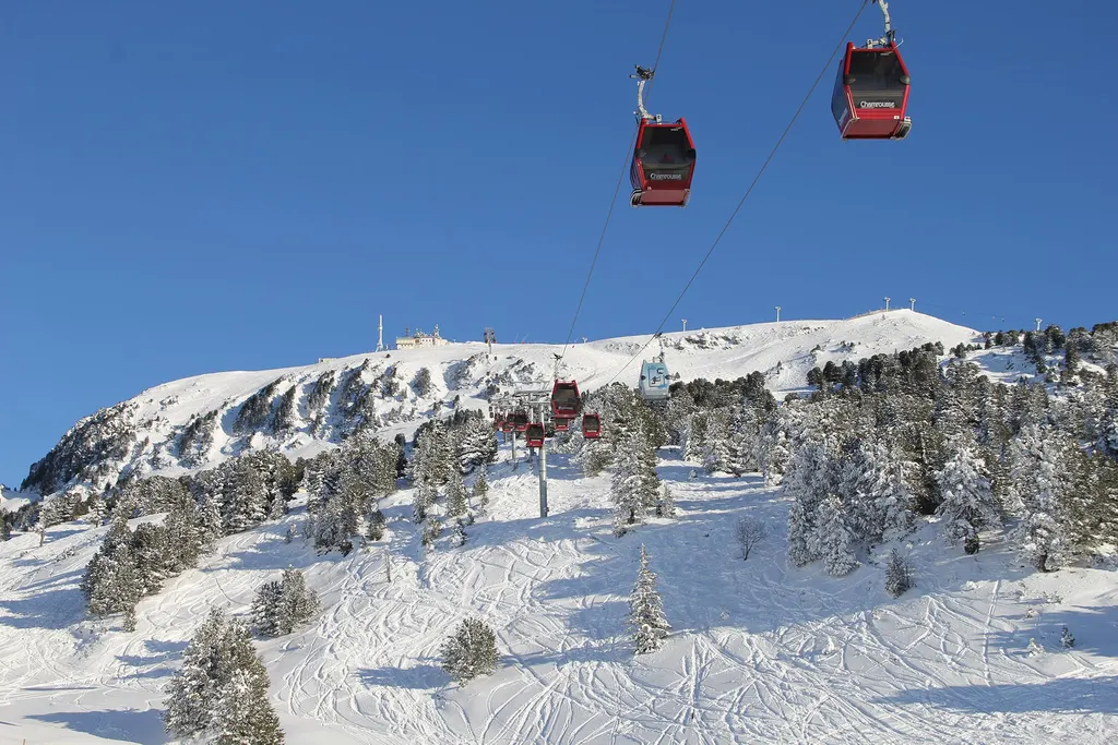 Gondole kolejki nad ośnieżonymi stokami Chamrousse, w tle szczyt Croix de Chamrousse