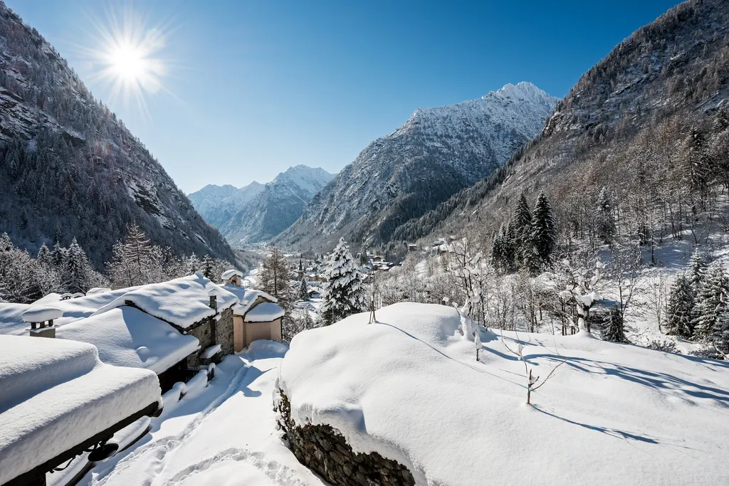 Zasypane śniegiem kamienne domy walserskie w Alagna Valsesia, w tle ośnieżone szczyty doliny Sesii