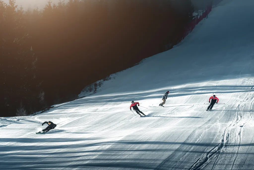 Narciarze na ratrakowanej trasie Ski&Sun w Świeradowie-Zdroju wśród lasu Gór Izerskich w porannym słońcu