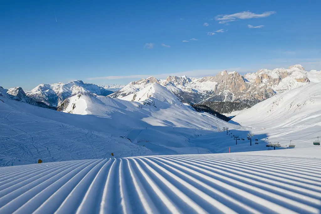 Wyratrakowana trasa Ciampac nad Alba di Canazei, w tle ośnieżone Dolomity z wyciągami na zboczu