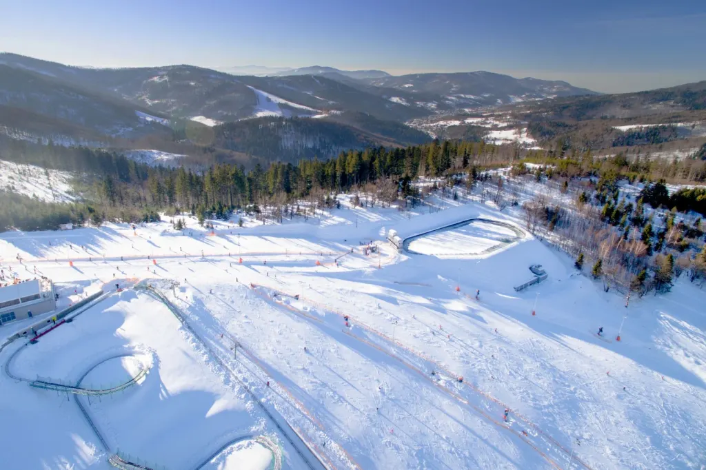 Ośnieżone stoki Beskid Sport Arena w Szczyrku z lotu ptaka, w tle zalesione pasma Beskidu Śląskiego