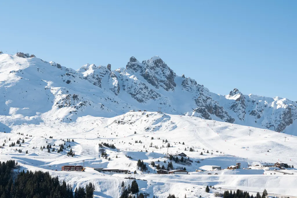 Ośnieżone stoki sektora altiportu w Courchevel z chatami, nad nimi skaliste szczyty Vanoise