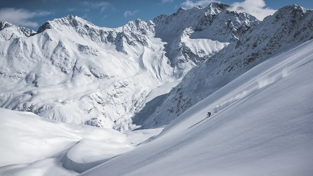 Zaśnieżone zbocza Kaunertaler Gletscher z małym narciarzem, w tle skaliste szczyty Alp Ötztalskich