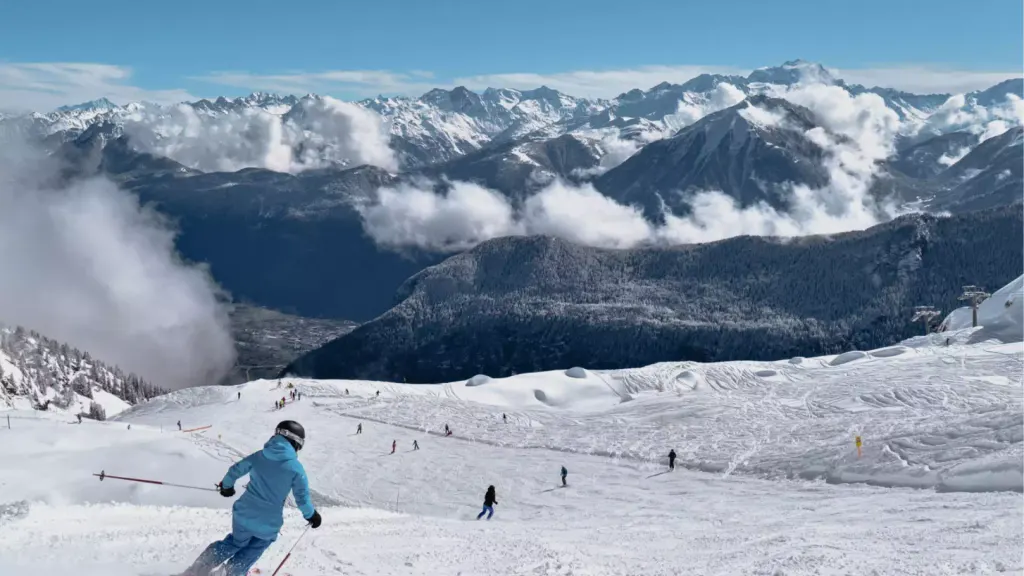 Trasa La Creusaz nad Les Marécottes z narciarzami, w tle chmury nad doliną i ośnieżone Alpy Walijskie