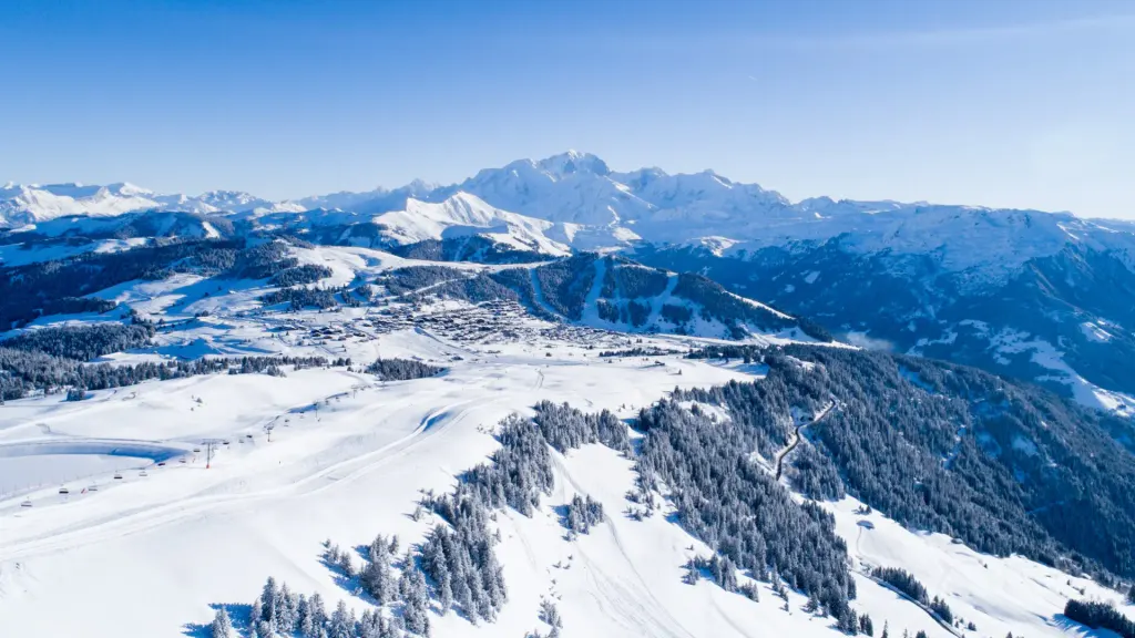 Les Saisies z lotu ptaka zimą, stoki i wyciągi wśród świerków, w tle masyw Mont Blanc