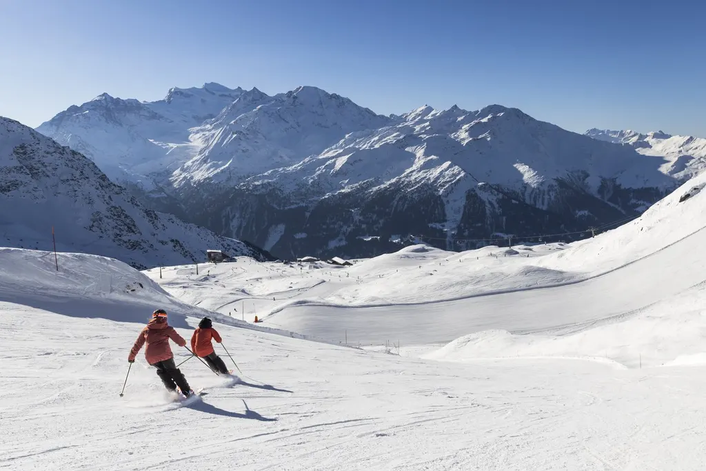 Dwoje narciarzy na szerokiej trasie w Verbier, w tle ośnieżony masyw Grand Combin