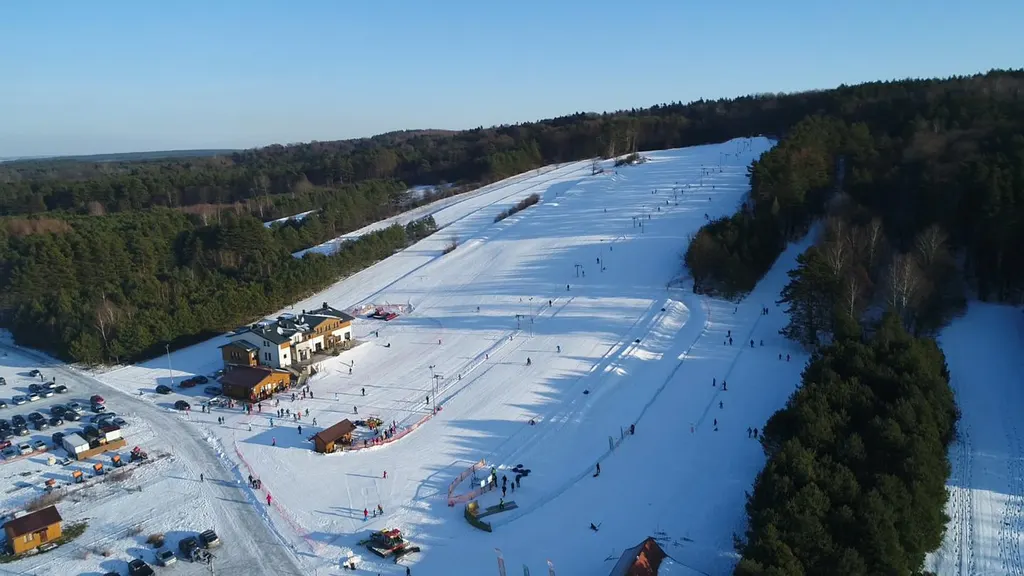 Stok narciarski w Jacni z lotu ptaka, ośnieżona trasa wśród sosnowych lasów Roztocza i budynek ośrodka