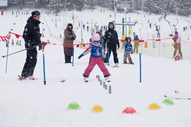 Dziewczynka w kasku pokonuje slalom z tyczek na oślej łączce, obok instruktor i rodzice