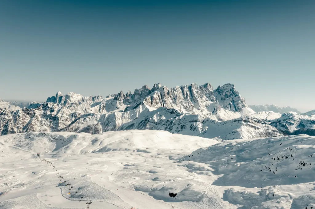 Zaśnieżone stoki i wyciągi Ski Area San Pellegrino zimą, w tle poszarpane szczyty Dolomitów