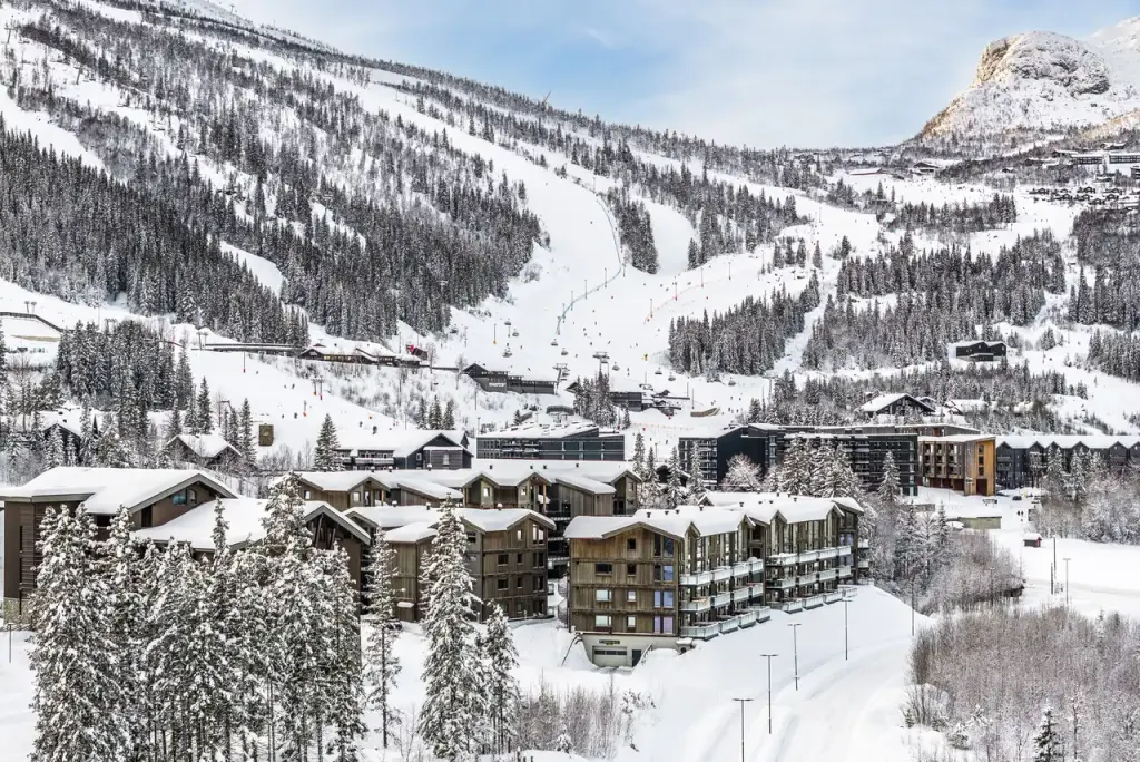 Trasy i wyciąg Hemsedal Skisenter nad ośnieżonymi apartamentami u podnóża stoku, wokół zaśnieżony las